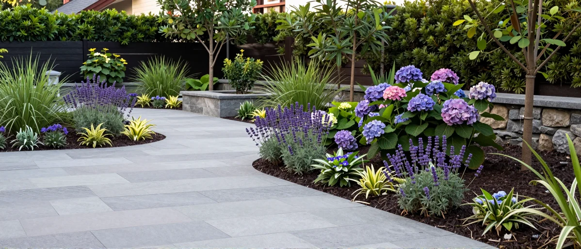 Frisch bepflanztes Gartenbeet neben einer Terrasse mit Lavendel, Hortensien, Straeuchern und Ziergraesern
