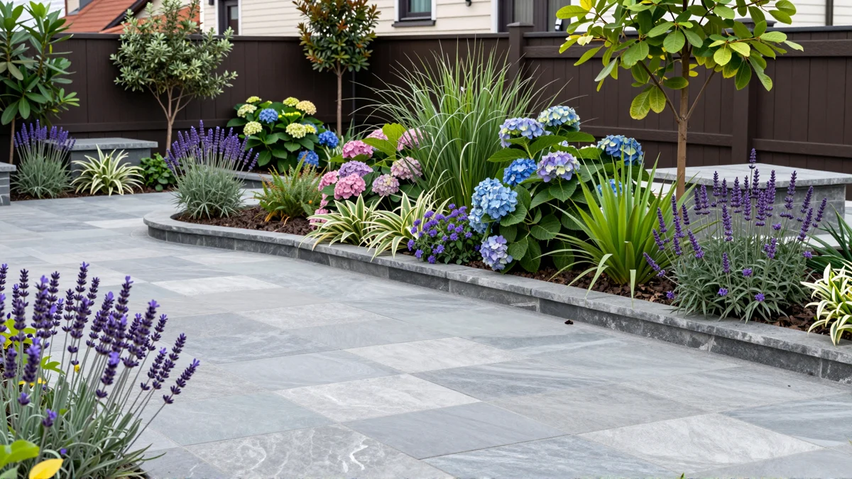 Frisch bepflanztes Gartenbeet neben einer Terrasse mit Lavendel, Hortensien, Straeuchern und Ziergraesern